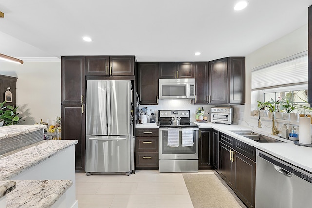 kitchen with dark brown cabinetry, sink, light stone counters, stainless steel appliances, and backsplash