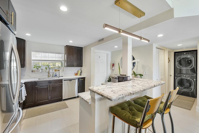 kitchen with stainless steel appliances, a breakfast bar, sink, and stacked washer / drying machine