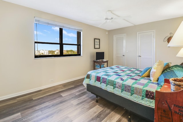 bedroom with hardwood / wood-style flooring, ceiling fan, and two closets