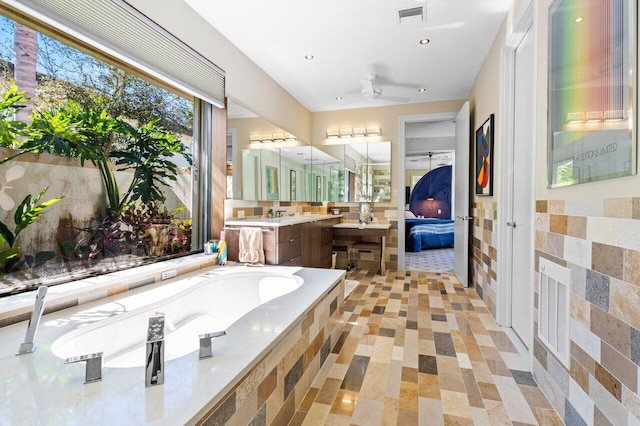 bathroom featuring tiled tub, vanity, tile walls, and ceiling fan