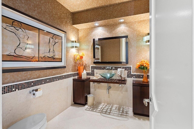 bathroom with tile patterned floors, toilet, sink, and tile walls