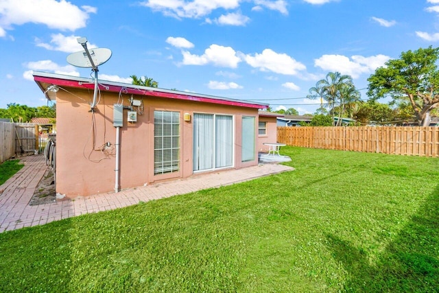 rear view of house featuring fence private yard, a yard, and stucco siding