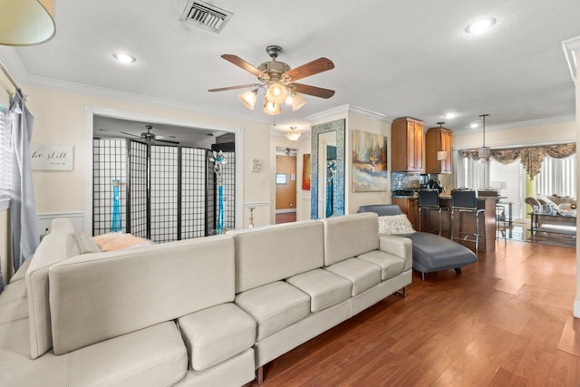 living room with ornamental molding, visible vents, ceiling fan, and wood finished floors