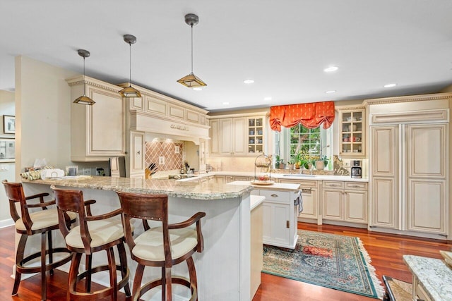 kitchen with light stone counters, light hardwood / wood-style flooring, hanging light fixtures, paneled built in fridge, and cream cabinetry