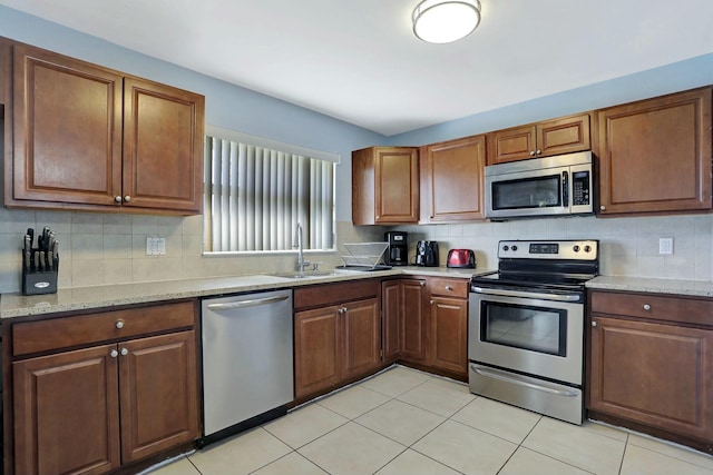 kitchen featuring light stone counters, stainless steel appliances, sink, and decorative backsplash