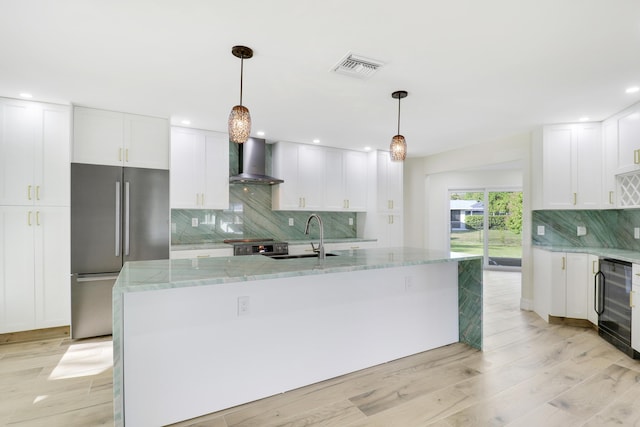 kitchen featuring stainless steel appliances, a sink, visible vents, wall chimney exhaust hood, and wine cooler