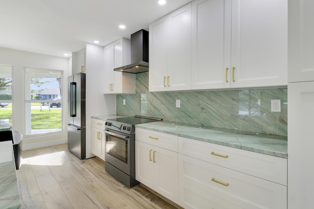 kitchen featuring light wood finished floors, backsplash, wall chimney range hood, white cabinets, and appliances with stainless steel finishes