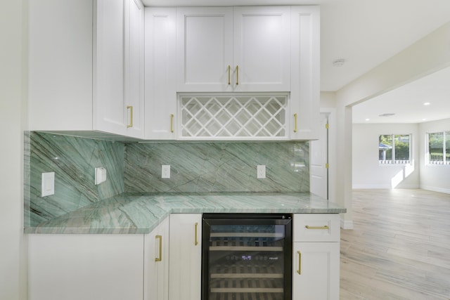 bar with a dry bar, tasteful backsplash, light wood-type flooring, beverage cooler, and baseboards