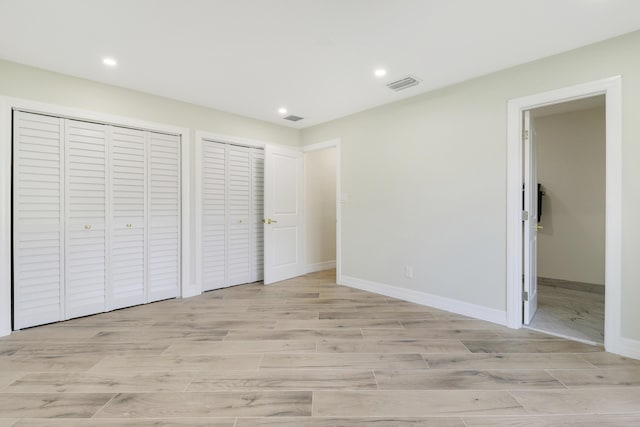 unfurnished bedroom with baseboards, light wood-style flooring, visible vents, and two closets