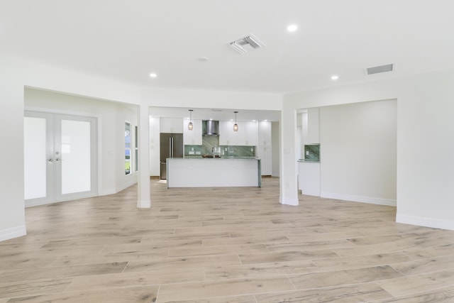 unfurnished living room with light wood-style flooring, visible vents, and french doors