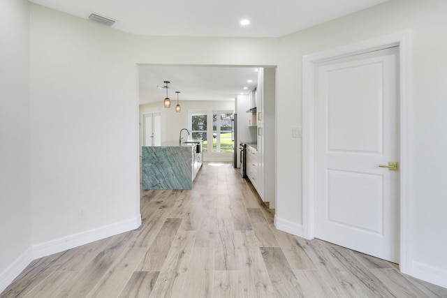 hallway with recessed lighting, visible vents, light wood-style floors, a sink, and baseboards