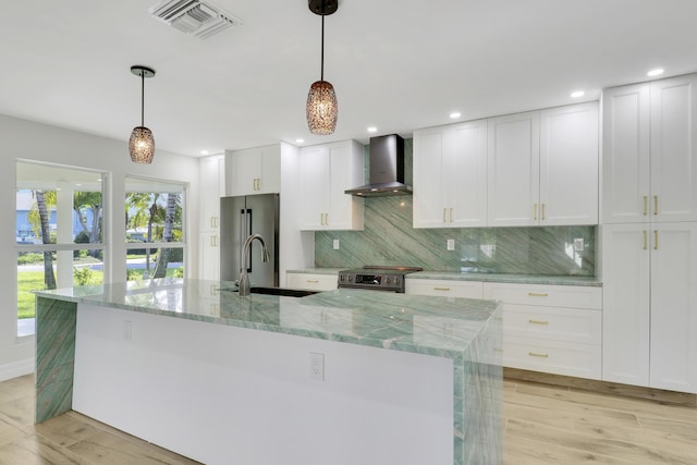 kitchen featuring a sink, visible vents, appliances with stainless steel finishes, wall chimney exhaust hood, and light wood finished floors