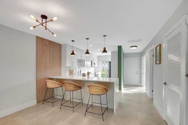 kitchen featuring tasteful backsplash, light countertops, a peninsula, a kitchen bar, and fridge