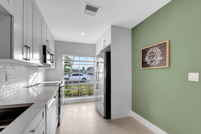 kitchen featuring light tile patterned floors, stainless steel appliances, light stone countertops, white cabinets, and decorative backsplash