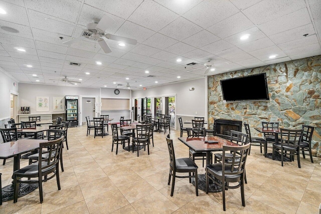 dining space featuring a stone fireplace, a paneled ceiling, ceiling fan, and light tile patterned floors