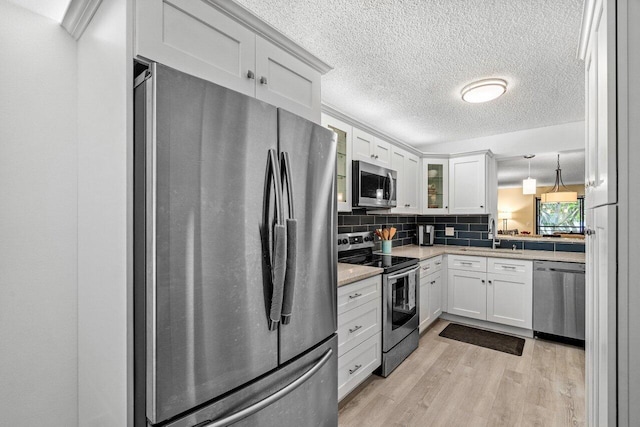 kitchen featuring appliances with stainless steel finishes, pendant lighting, sink, white cabinets, and light hardwood / wood-style floors