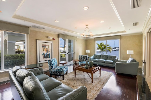 living room with dark hardwood / wood-style floors, ornamental molding, a tray ceiling, a water view, and an inviting chandelier