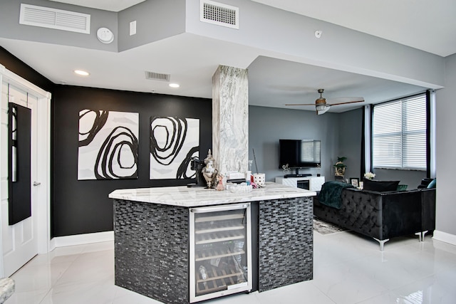 kitchen featuring wine cooler, ceiling fan, a center island, and light stone countertops