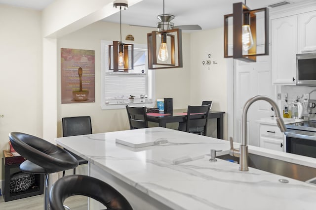 kitchen featuring pendant lighting, sink, white cabinets, decorative backsplash, and light stone counters