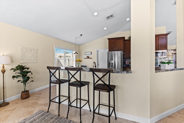 kitchen featuring lofted ceiling, a breakfast bar, hanging light fixtures, appliances with stainless steel finishes, and kitchen peninsula