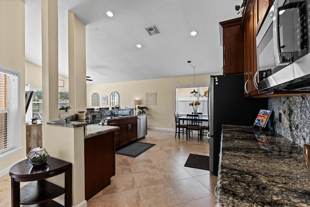 kitchen with appliances with stainless steel finishes, dark stone counters, light tile patterned floors, dark brown cabinetry, and kitchen peninsula