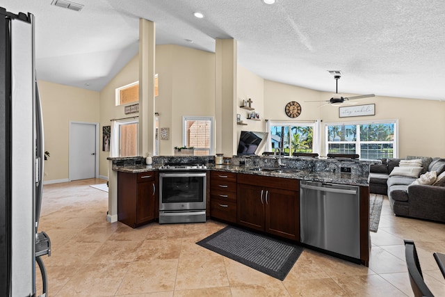 kitchen featuring stainless steel appliances, vaulted ceiling, sink, and dark stone countertops