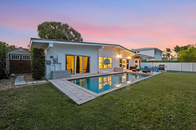 back house at dusk featuring an outdoor living space, a patio, a shed, and a lawn