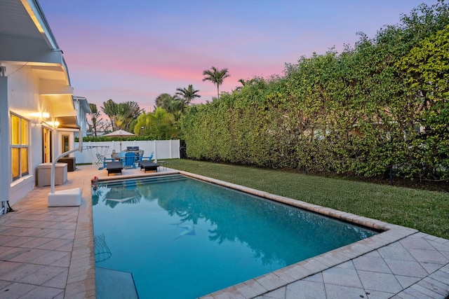 pool at dusk featuring a yard and a patio