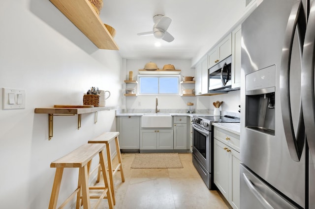 kitchen featuring open shelves, gray cabinets, light countertops, appliances with stainless steel finishes, and a sink