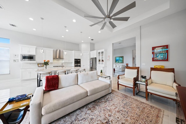 tiled living room with a raised ceiling, ceiling fan, and a high ceiling