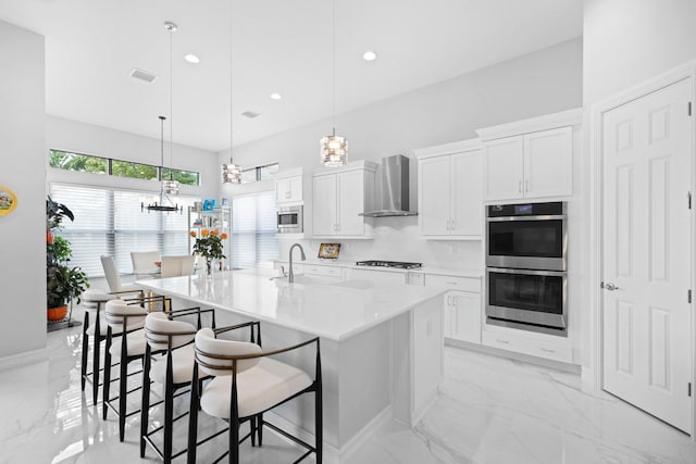 kitchen with white cabinets, decorative light fixtures, an island with sink, and wall chimney exhaust hood