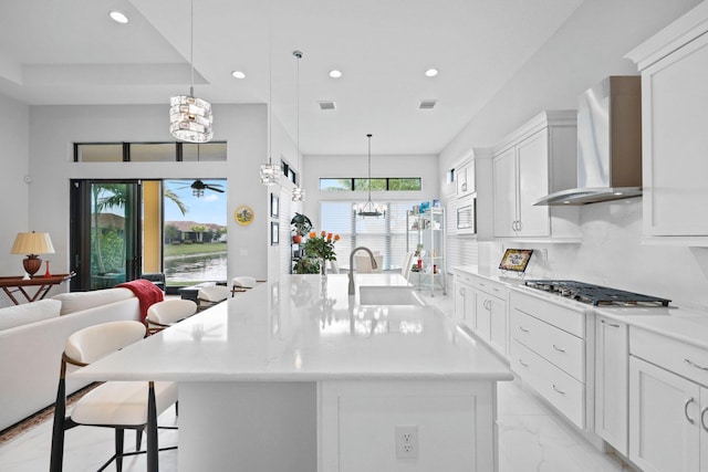 kitchen featuring an island with sink, decorative light fixtures, sink, and wall chimney range hood