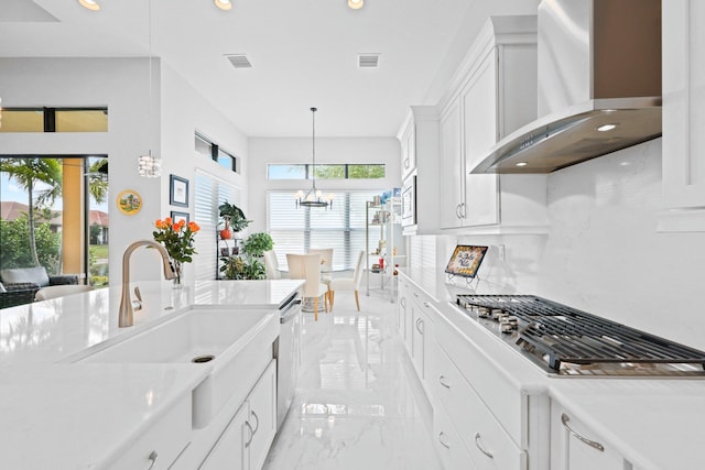 kitchen with wall chimney range hood, plenty of natural light, stainless steel appliances, white cabinets, and decorative light fixtures