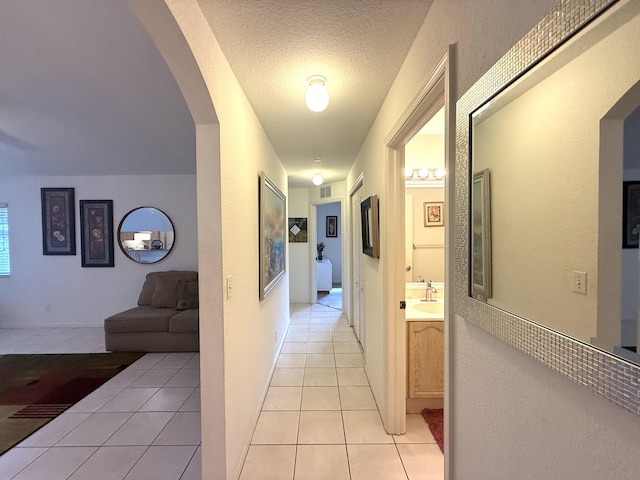 corridor featuring light tile patterned flooring, sink, and a textured ceiling