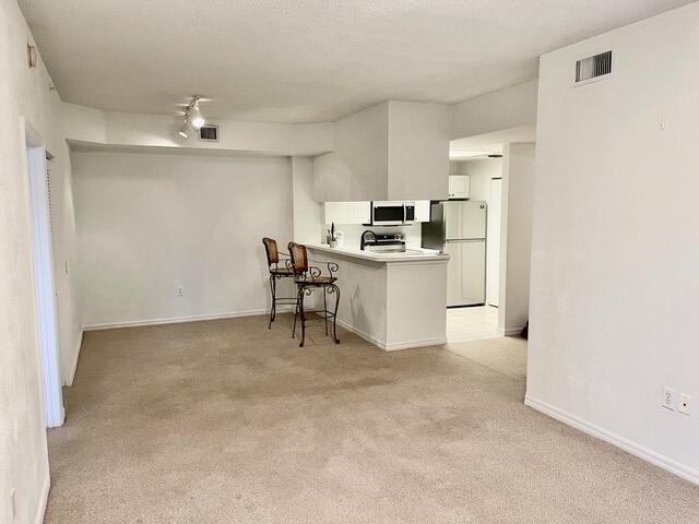 kitchen featuring light colored carpet, visible vents, freestanding refrigerator, a peninsula, and a kitchen breakfast bar