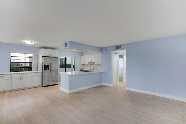 kitchen featuring stainless steel refrigerator with ice dispenser, white cabinetry, tasteful backsplash, kitchen peninsula, and a healthy amount of sunlight