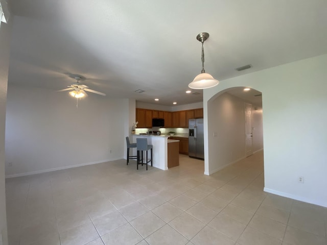 kitchen with stainless steel refrigerator with ice dispenser, a breakfast bar area, light tile patterned floors, pendant lighting, and ceiling fan