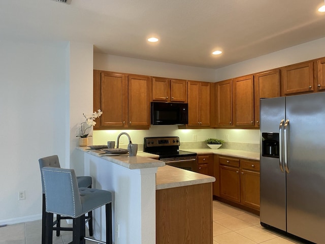 kitchen with light tile patterned flooring, stainless steel appliances, a kitchen bar, and kitchen peninsula