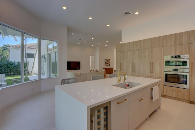 kitchen with sink, beverage cooler, a kitchen island with sink, plenty of natural light, and stainless steel double oven