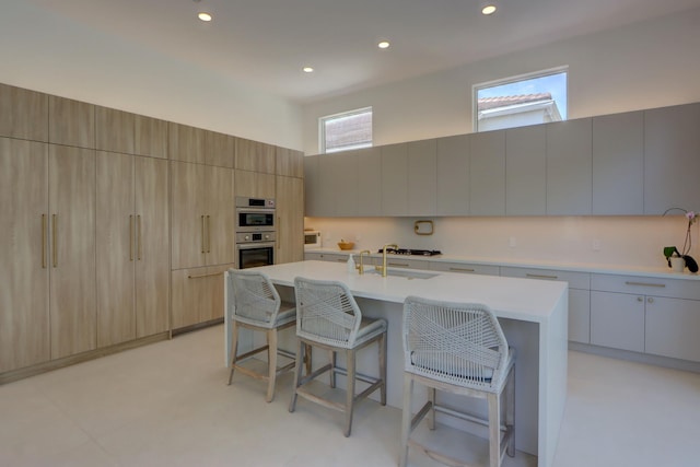 kitchen with sink, a breakfast bar area, a high ceiling, a center island with sink, and light brown cabinetry