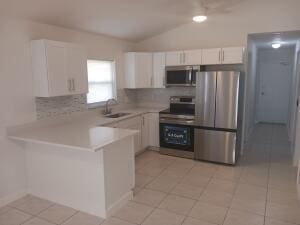 kitchen featuring sink, kitchen peninsula, white cabinets, stainless steel appliances, and backsplash