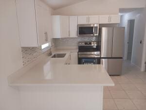 kitchen featuring sink, white cabinetry, backsplash, stainless steel appliances, and kitchen peninsula