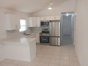 kitchen featuring lofted ceiling, sink, stainless steel appliances, white cabinets, and decorative backsplash