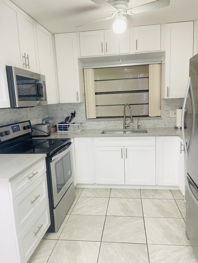 kitchen featuring light tile patterned floors, stainless steel appliances, tasteful backsplash, white cabinets, and a sink