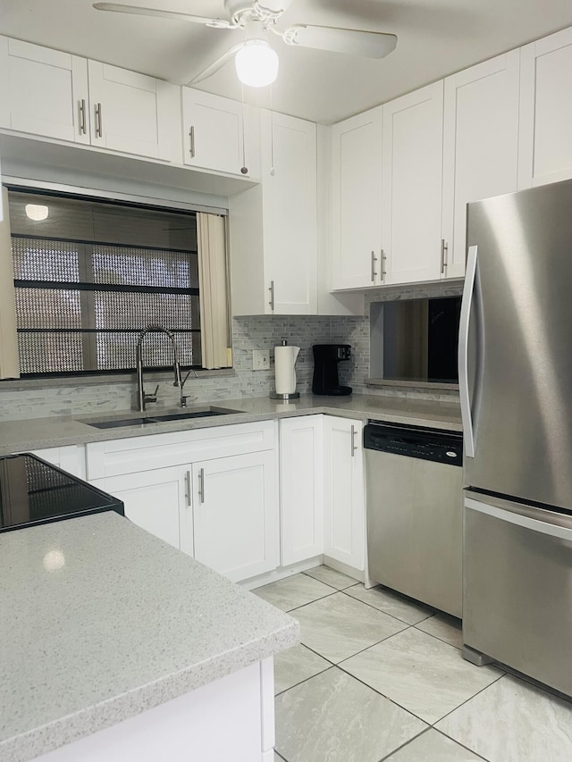 kitchen featuring stainless steel appliances, a sink, white cabinetry, a ceiling fan, and backsplash