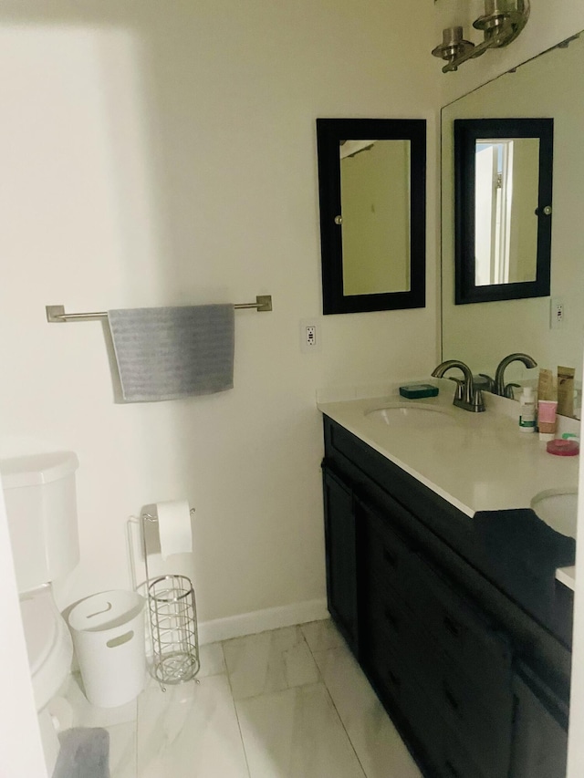 bathroom with marble finish floor, toilet, vanity, and baseboards