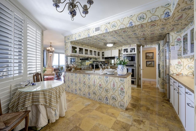 kitchen featuring appliances with stainless steel finishes, white cabinets, ornamental molding, kitchen peninsula, and an inviting chandelier