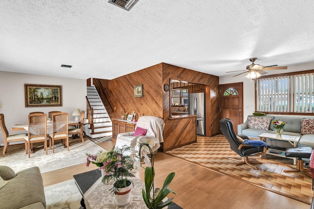 living room featuring ceiling fan, light wood-type flooring, a textured ceiling, and wood walls