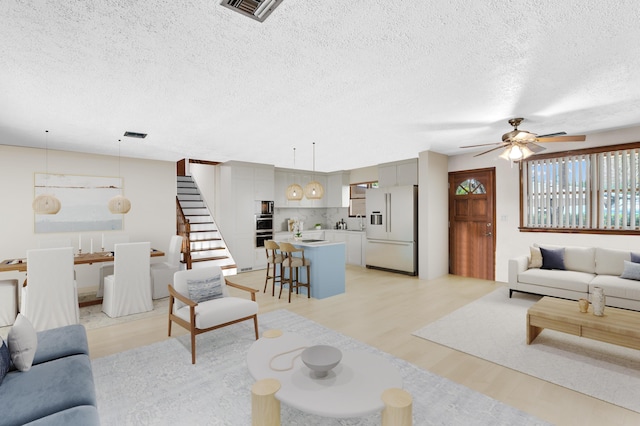 living room featuring ceiling fan, a textured ceiling, and light wood-type flooring