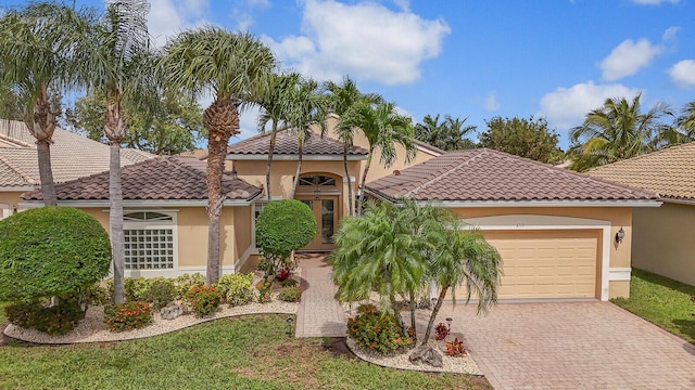 mediterranean / spanish house featuring decorative driveway, an attached garage, a tile roof, and stucco siding